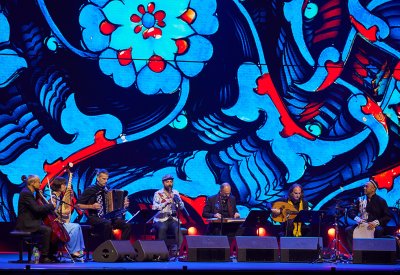Aga Khan Master Musicians with Vincent Peirani and Vincent Ségal playing in front of a bring blue backdrop