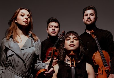 The members of Attacca String Quartet looking into the camera in front of a ombre gray backdrop