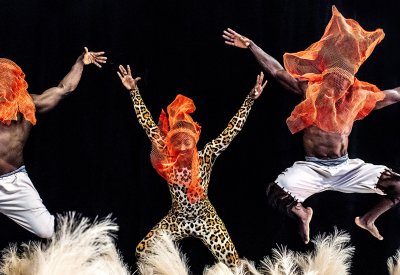 Dancers are jumping with their hands up in front of a black backdrop