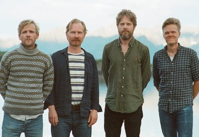 The members of the Danish String Quartet standing in front of a clear blue lake 
