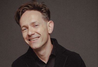 A man smiling at the camera in front of a gray background.