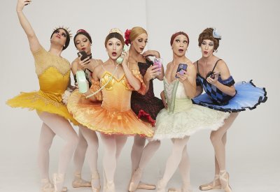 Members of the Les Ballets Trockadero de Monte Carlo in colorful ballet attire posing in front of a white backdrop