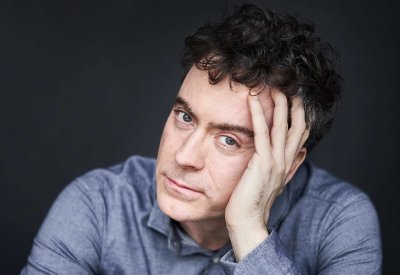 A portrait of Paul Lewis. He is wearing a navy shirt and is posing in front of a black background