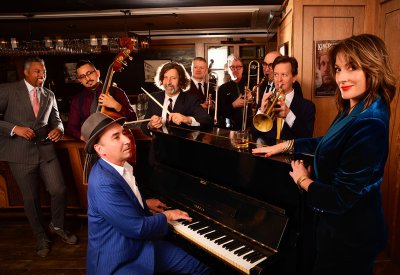 The band is standing around the piano posing in a cozy backdrop